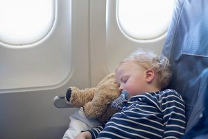 Bébé blond endormi sur sa peluche ours durant un vol en avion