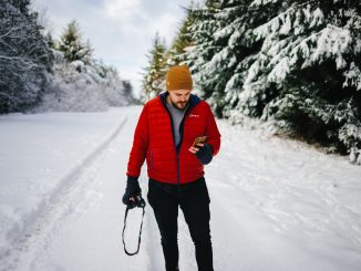 homme sur une route enneigées portant une doudoune rouge un bonnet jaune et un pantalon noir