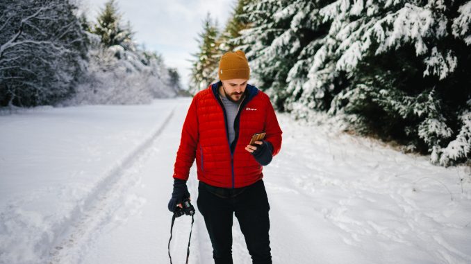 homme-hiver homme sur une route enneigées portant une doudoune rouge un bonnet jaune et un pantalon noir